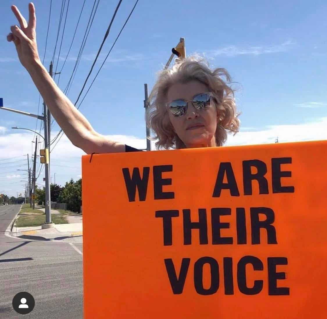 An activist bearing witness at a slaughterhouse vigil, holding a sign 'We are their voice'